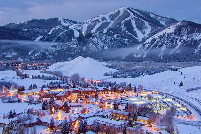 A mountain town glowing with lights at blue hour beneath a lit ski hill