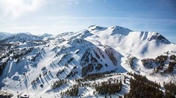 Wide view of a snow-covered ridgeline with groomed runs cut through the trees